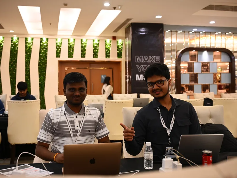 Mirza pointing at a teammate as they sit at their laptops in the hall