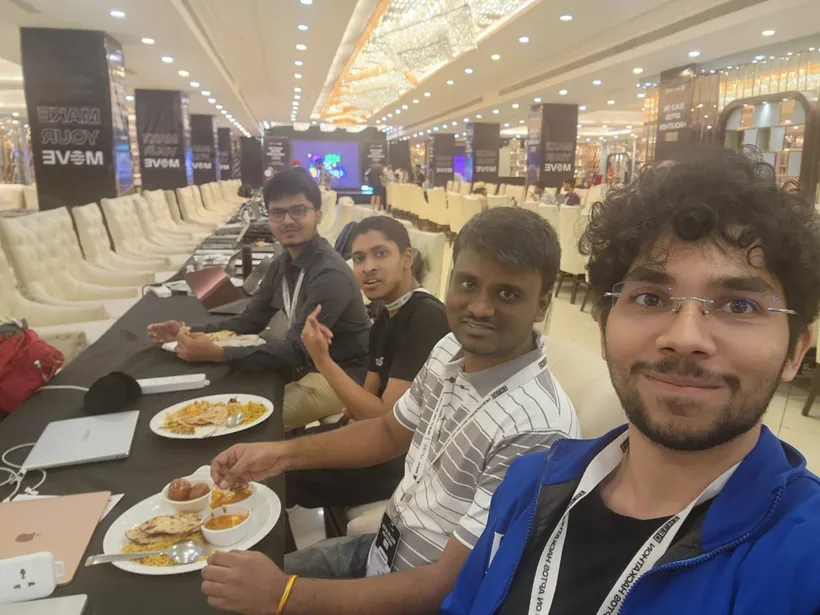 A selfie of the team eating lunch at the hacking table, with Make Your Move pillars behind