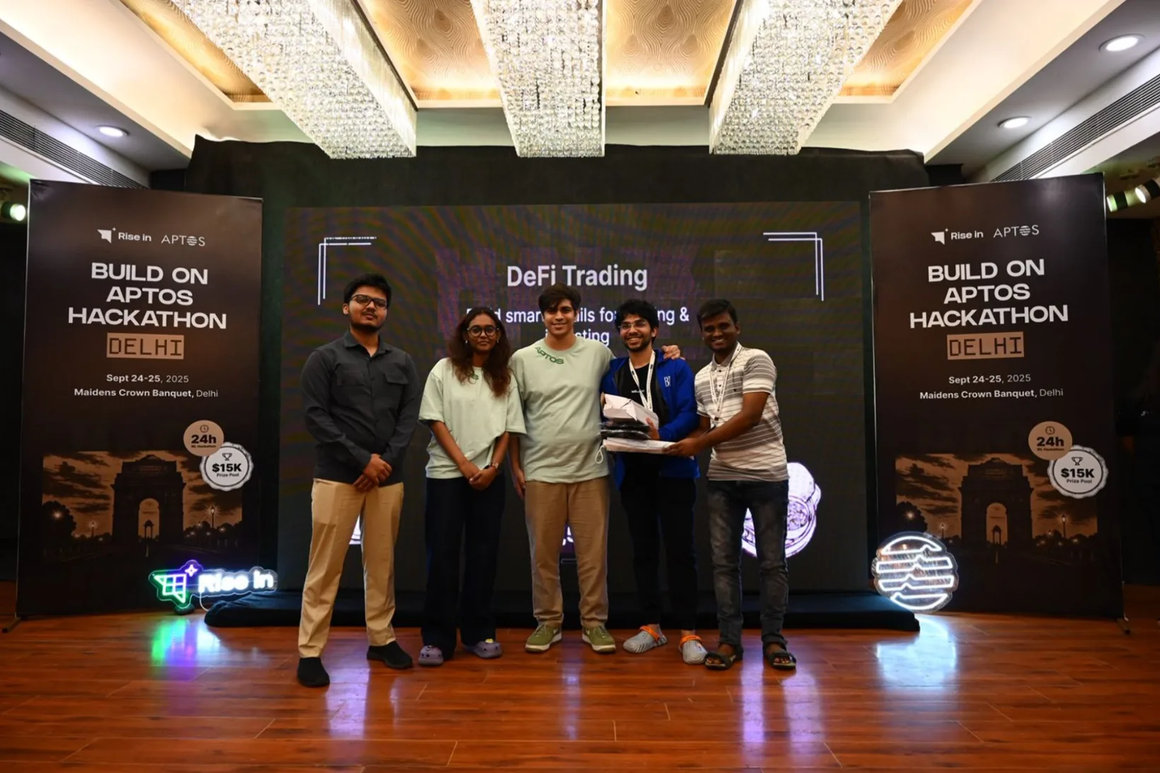 Mirza and his teammates on stage receiving second place in the DeFi trading track, between two Build on Aptos Hackathon Delhi banners