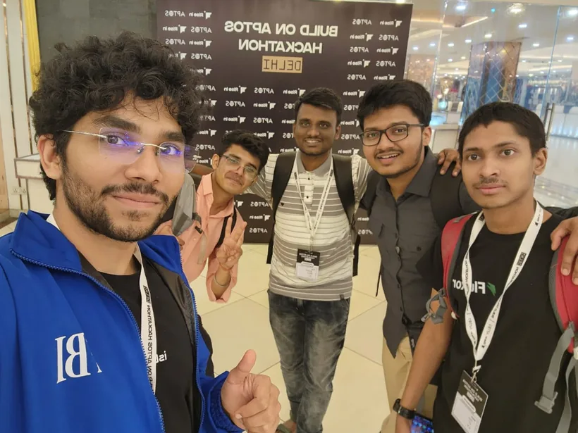 A selfie of Mirza with teammates and friends in front of the Build on Aptos Hackathon backdrop