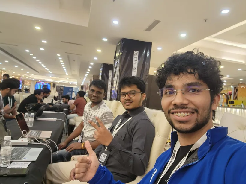 A selfie of a teammate giving a thumbs up, with Mirza making a peace sign beside him at the long hacking tables