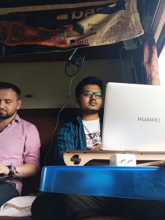 A hacker in a Blocktrain T-shirt coding on a laptop propped on a wooden lap desk in a train berth