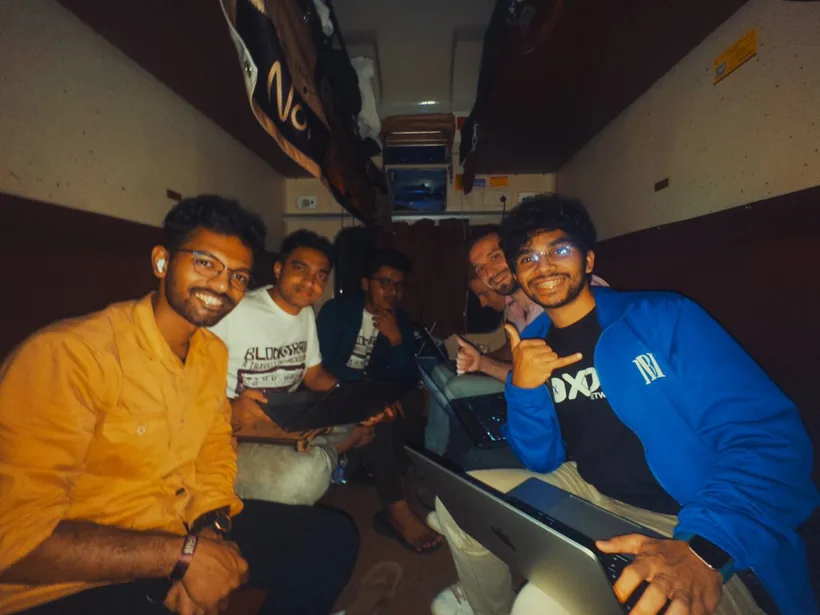 Hackers with laptops crowded into a train compartment at night, one flashing a shaka sign