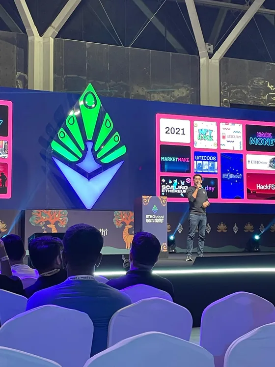 A speaker on stage at the opening, in front of a wall of past ETHGlobal events