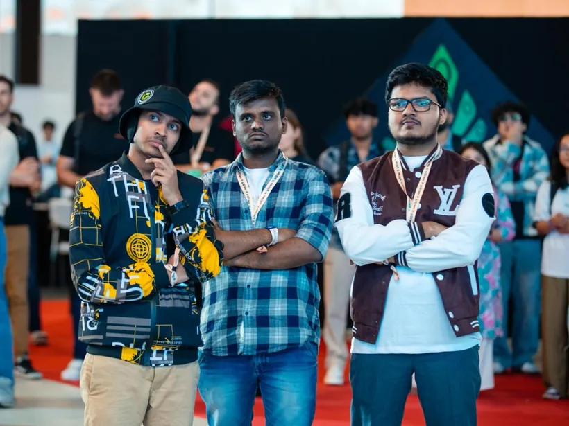 Mirza and two teammates, arms crossed, watching the stage